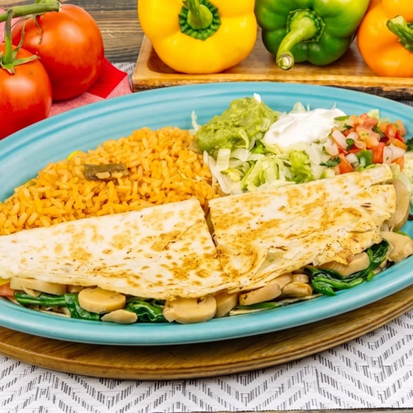 Vegetable quesadilla with rice, guacamole, sour cream, and pico de gallo on a blue plate.