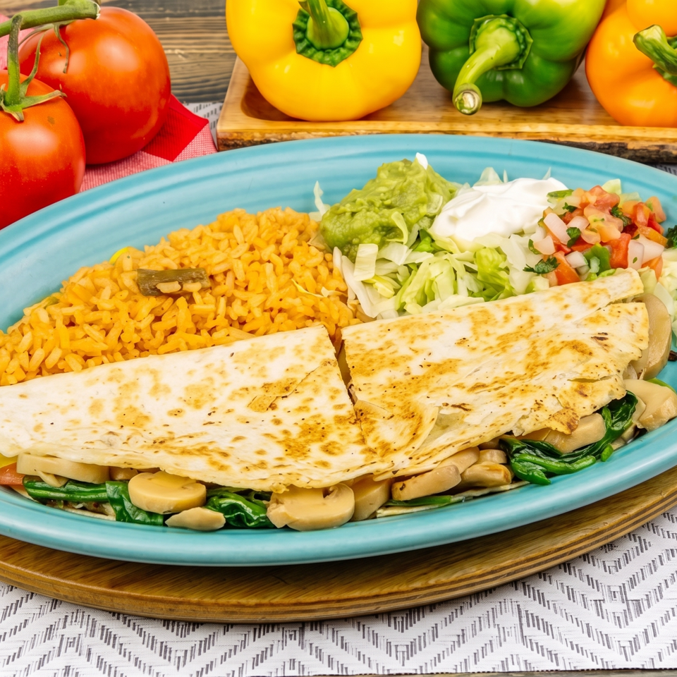 Vegetable quesadilla with rice, guacamole, sour cream, and pico de gallo on a blue plate.