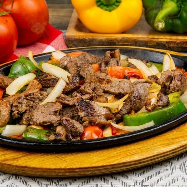 Sizzling beef fajitas with colorful bell peppers and onions in a cast iron skillet.