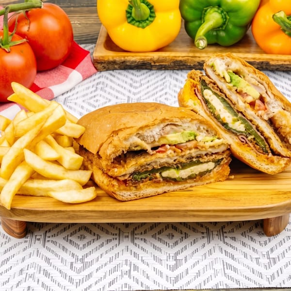 Two halves of a sandwich with avocado and jalapeños, fries, tomatoes, and bell peppers.