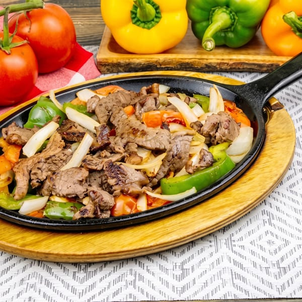Sizzling beef fajitas with bell peppers and onions in a cast iron skillet, surrounded by fresh vegetables.